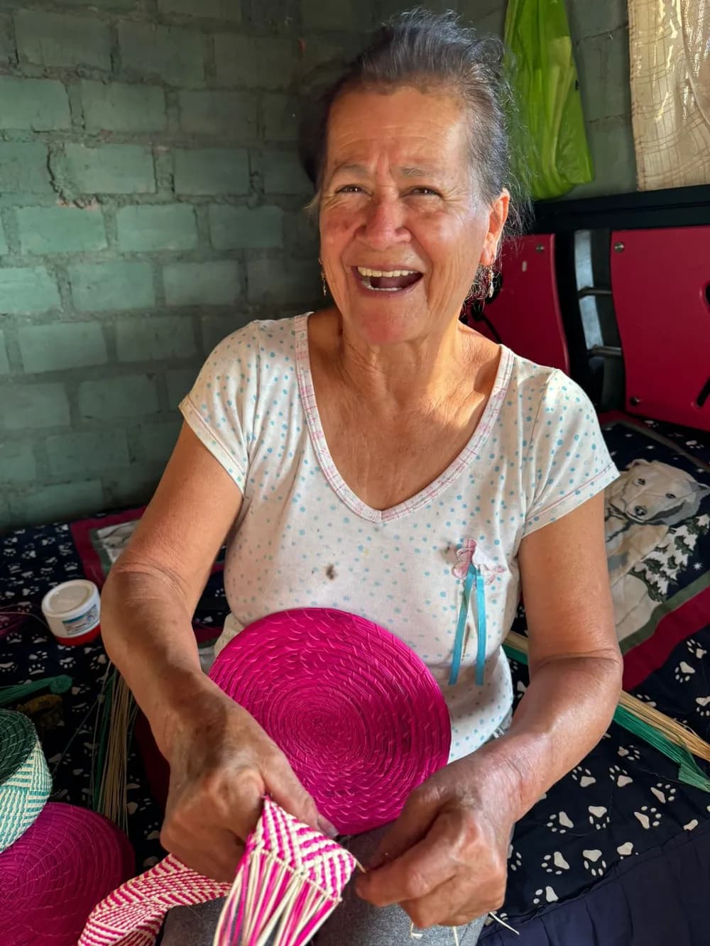 A Colombian artisan smiling as she weaves pink iraca palm